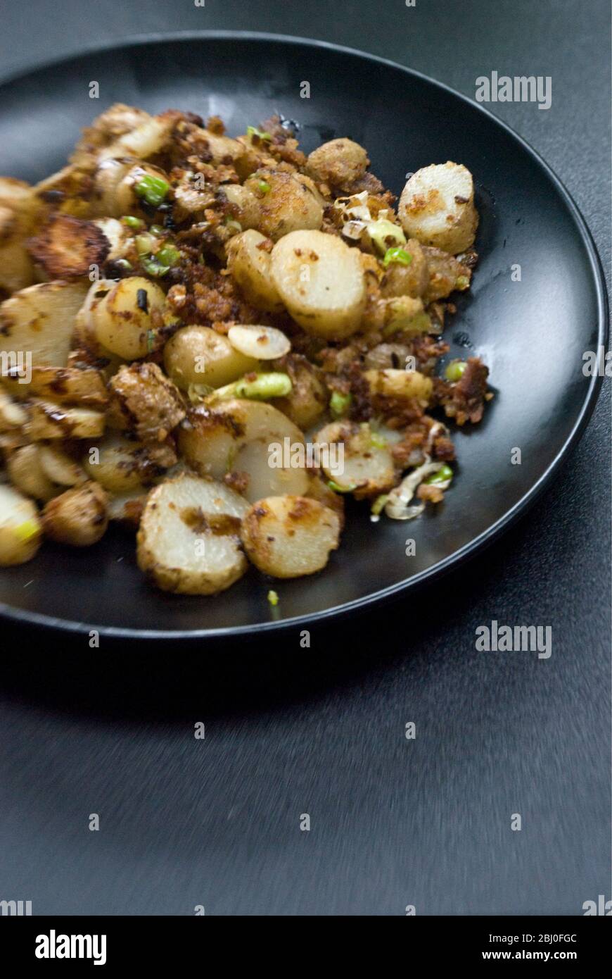 Dish of fried potatoes, sauteed with anchovies, spring onions and breadcrumbs. - Stock Photo