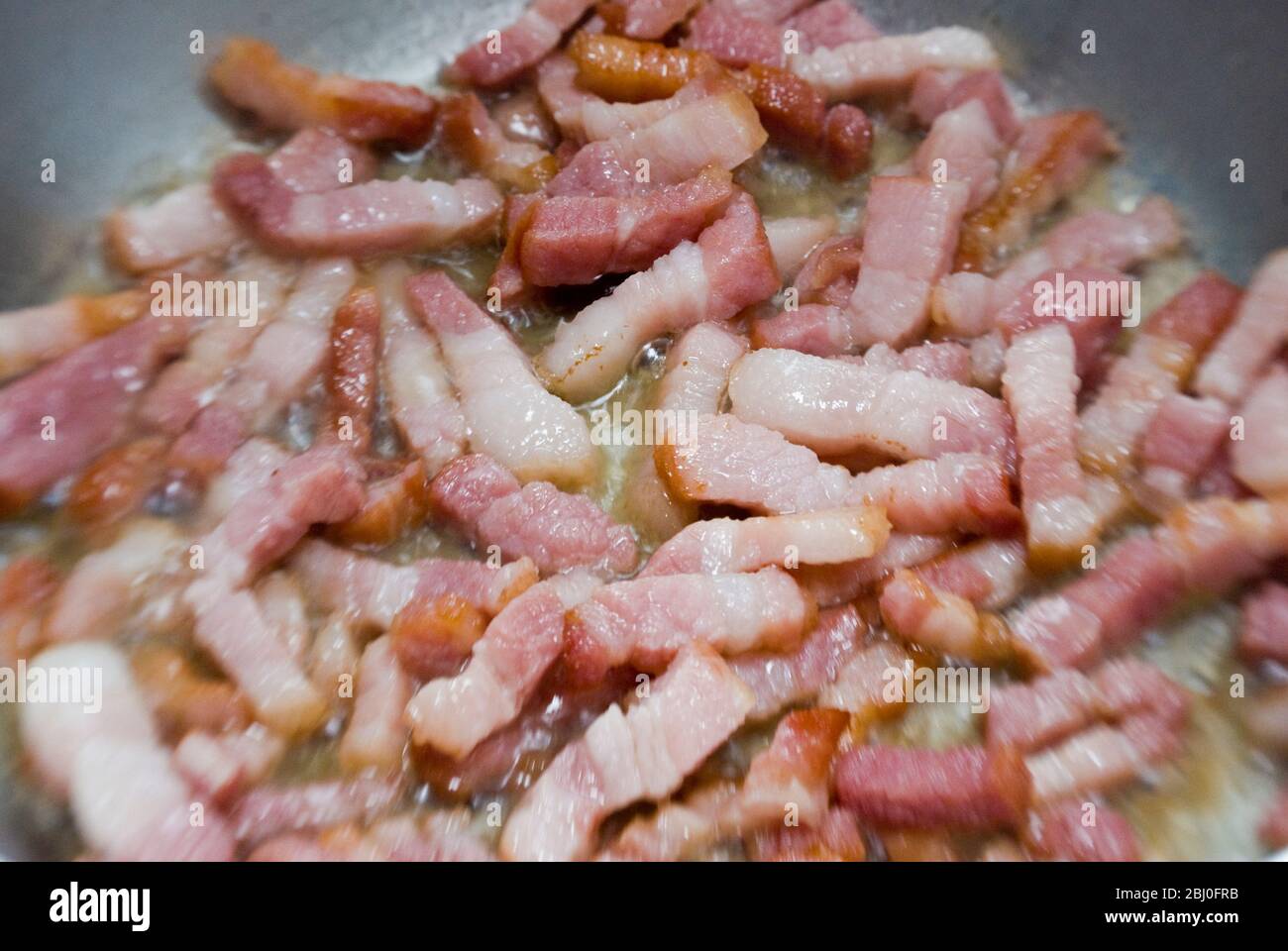 Cooking chopped pieces of streaky bacon in a frying pan. Known as pancetta in Italy and lardons in France - Stock Photo