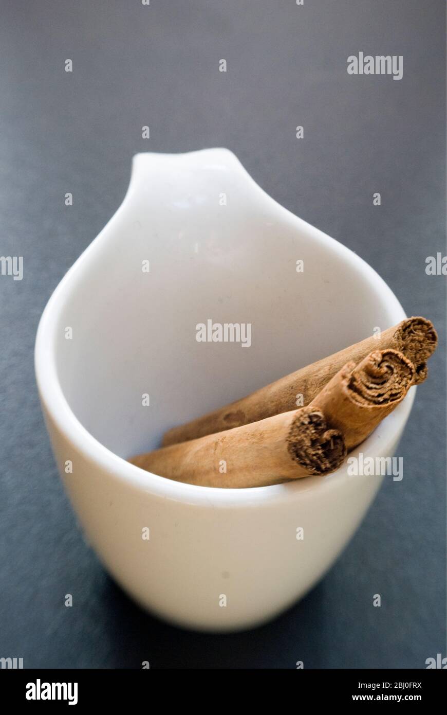 Sticks of cinnamon in small white cup - Stock Photo