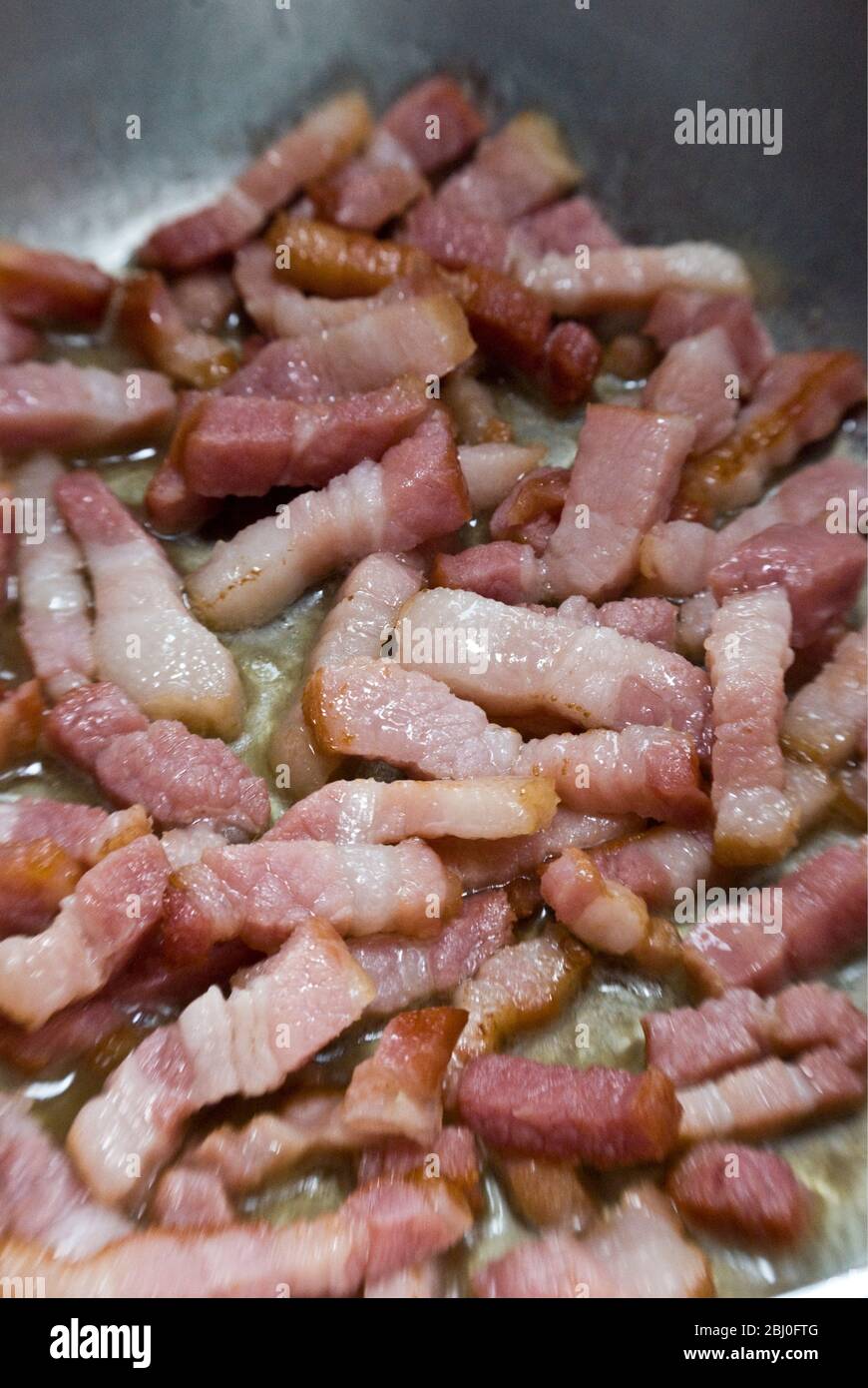 Cooking chopped pieces of streaky bacon in a frying pan. Known as pancetta in Italy and lardons in France - Stock Photo