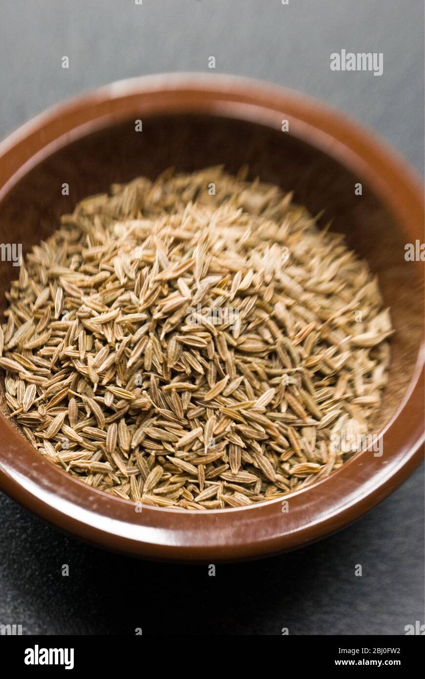 Whole dried cumin seeds in small bowl - Stock Photo
