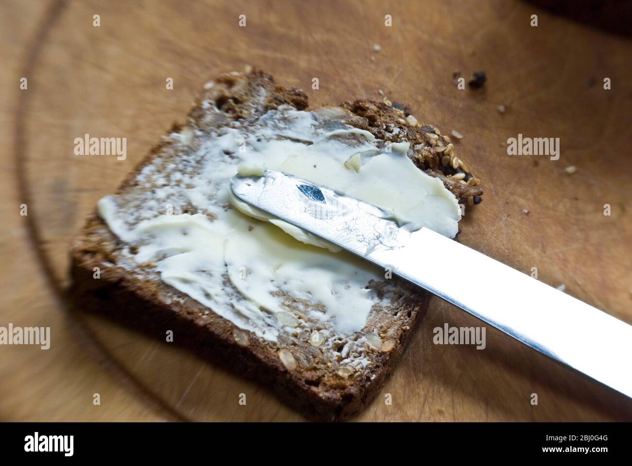 Spreading butter onto slice of Scandinavian style cparse rye bread. - Stock Photo