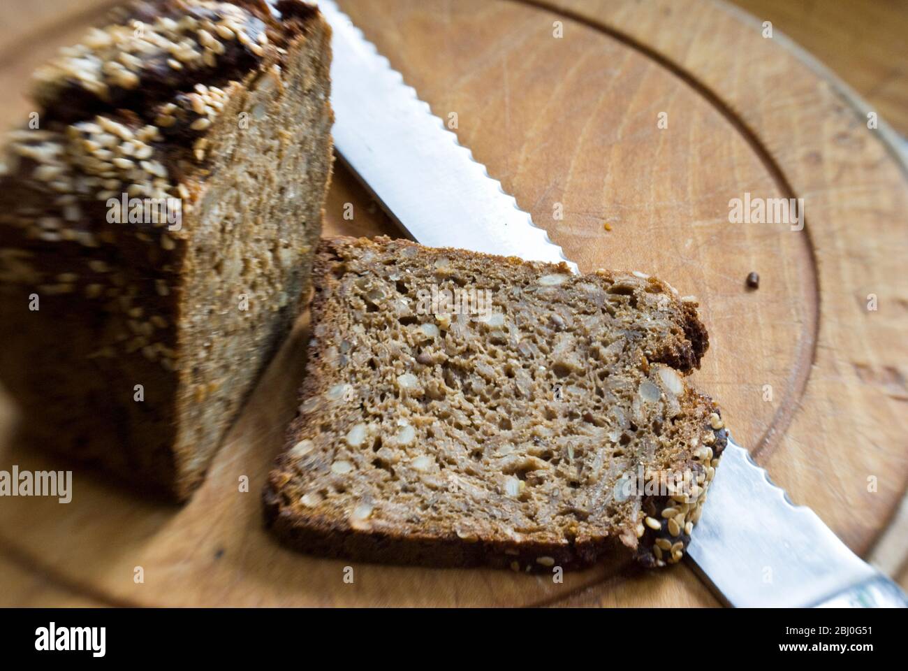 Slice of coarse, Scandinavian style rye bread on wooden bread board. - Stock Photo