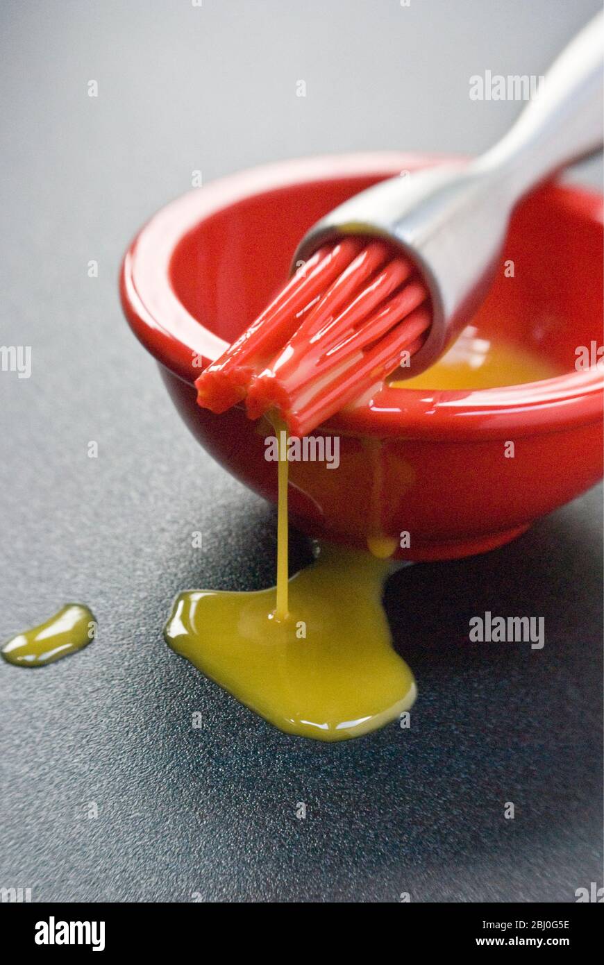 Egg yolk in small red bowl and dripping off red silicone 'bristles' of