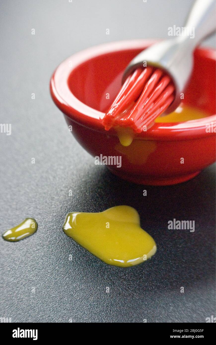 Egg yolk in small red bowl and dripping off red silicone 'bristles' of