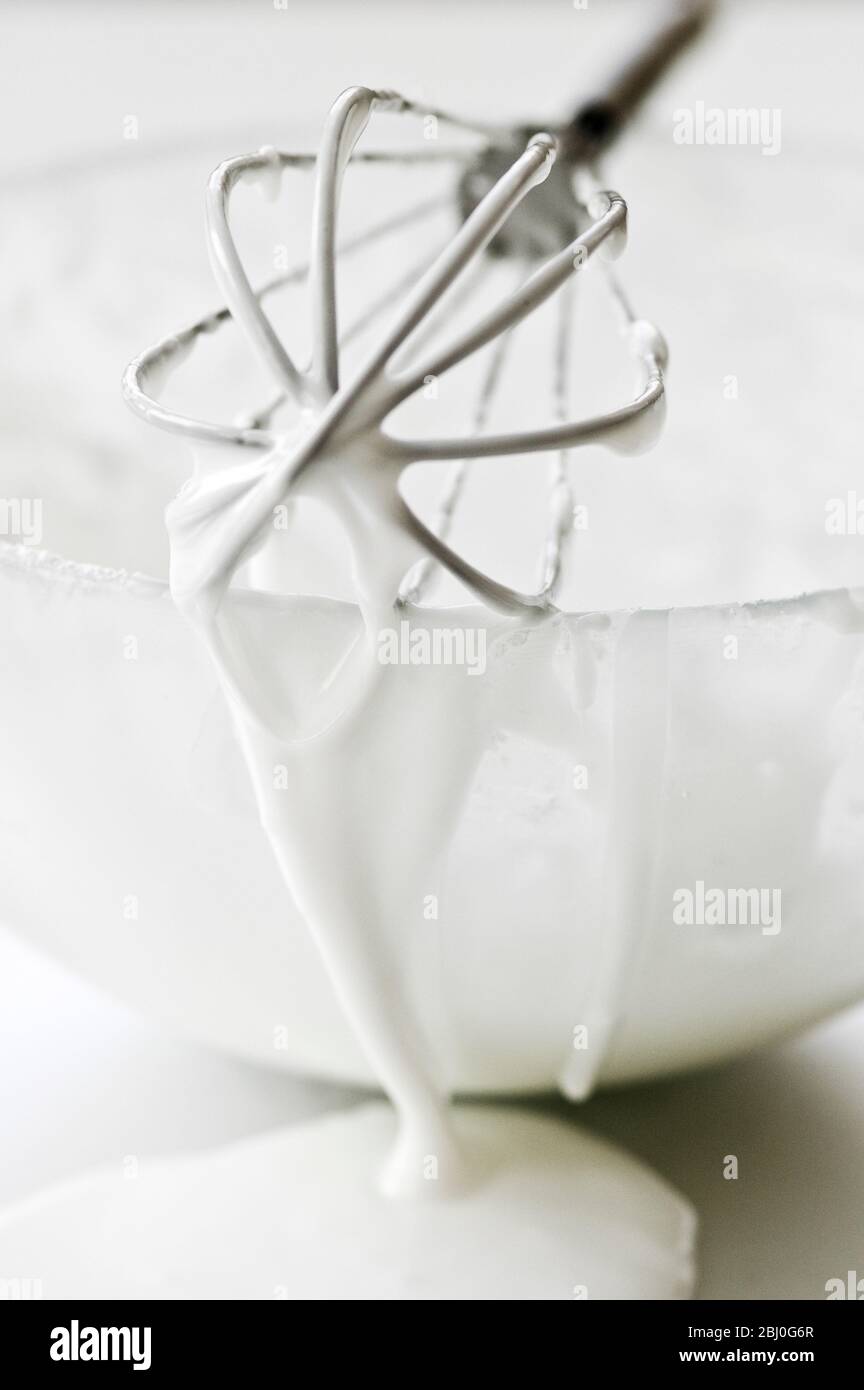 Bowl of white icing with dripping balloon whisk - Stock Photo