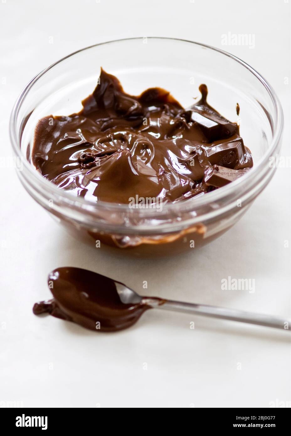 Glass bowl of melting chocolate with spoon on white surface - Stock Photo