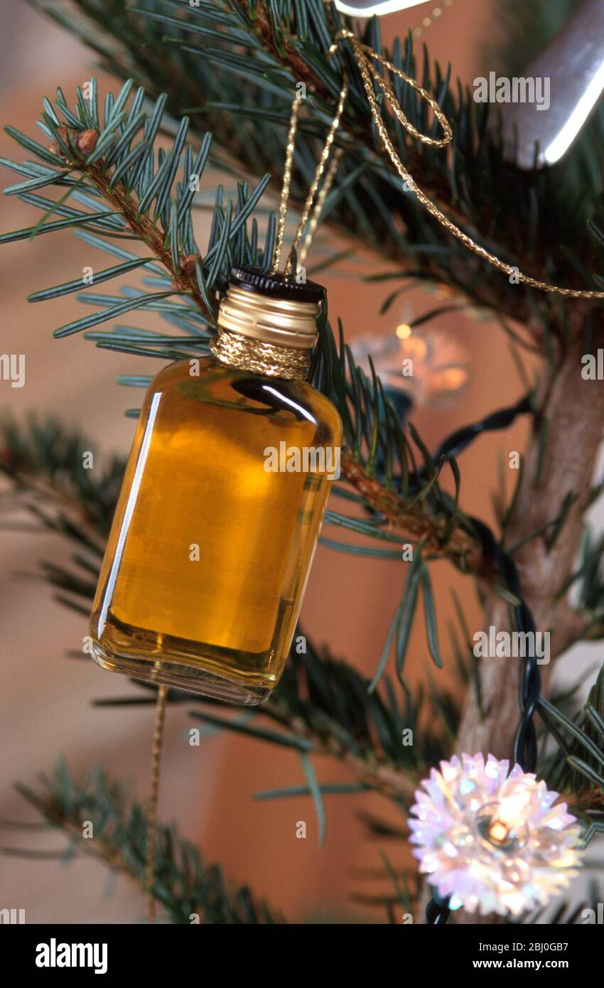 Miniature bottle of whisky tied on to Christmas tree as gift and decoration. - Stock Photo