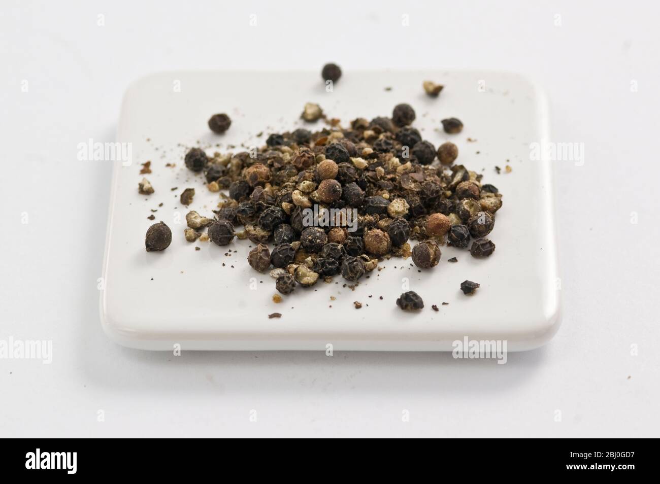 Lightly crushed black peppercorns on white surface Stock Photo