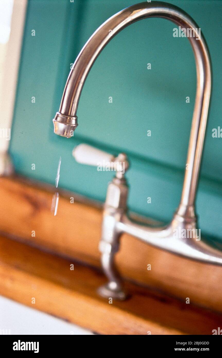 Modern high kitchen tap on retro style sink dripping slightly. - Stock Photo