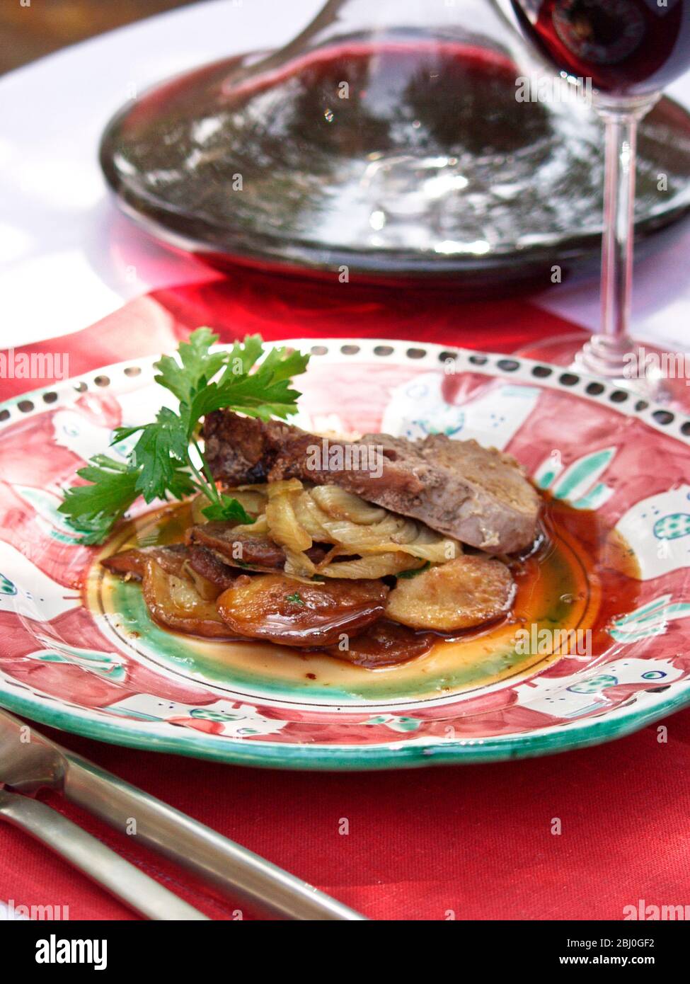 Pork loin wrapped in pancetta with onions and potatoes served on hand painted Italian plate outdoors - Stock Photo