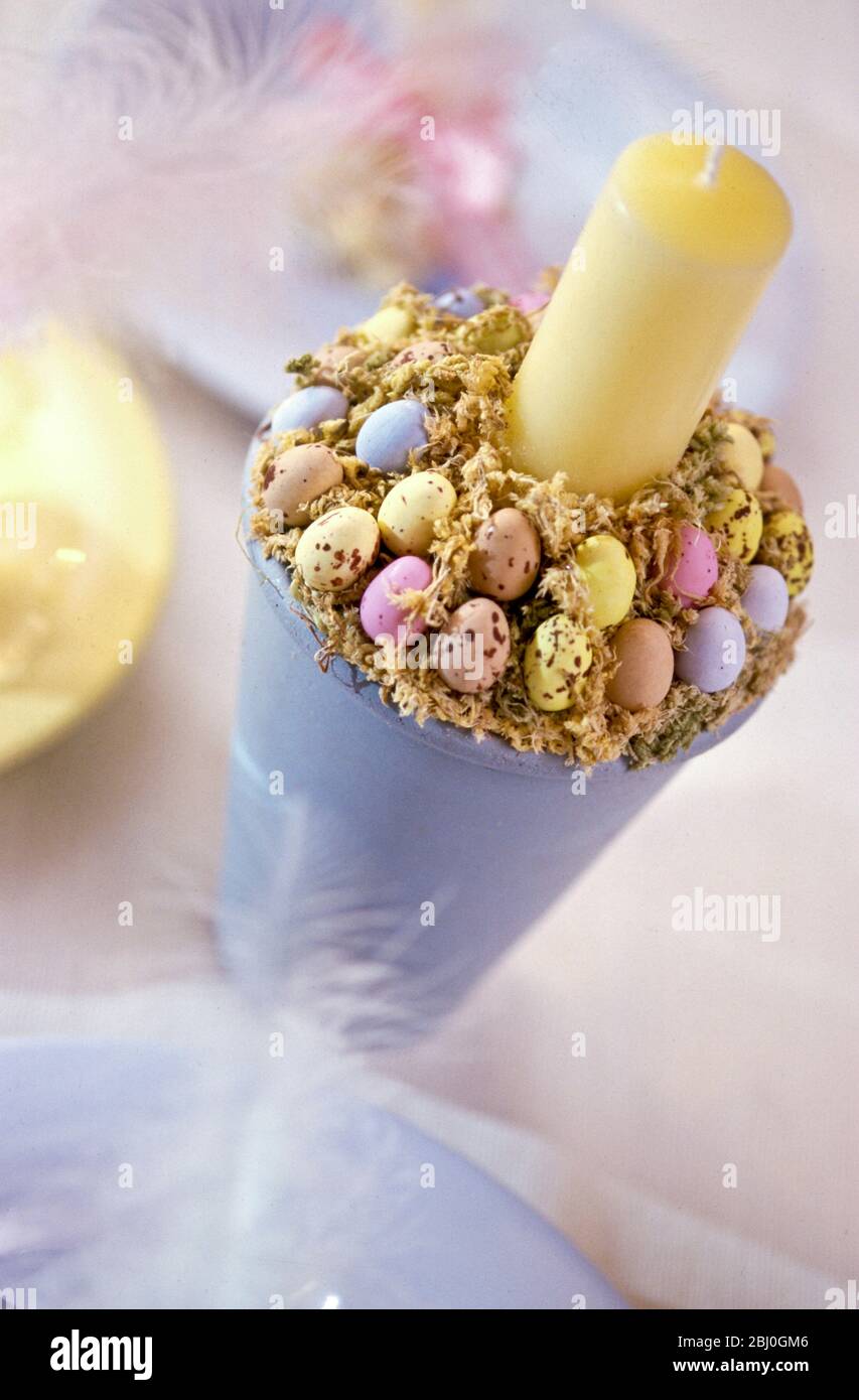 Pastel coloured easter decorations with painted tall pot decorated with sugar coated mini chocolate eggs surrouding candle - Stock Photo