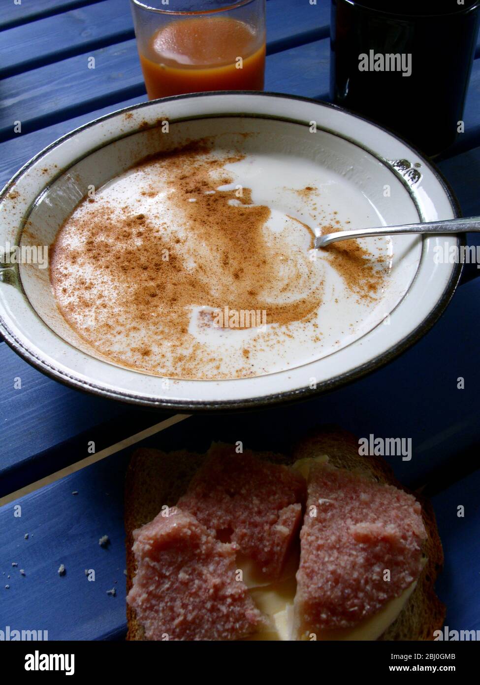 Swedish summer outdoor breakfast of filmjšlk with dusting of cinnamon, rosehip juice drink, and pork brawn on rye bread - Stock Photo