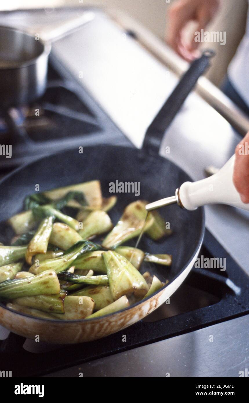 Stir frying chard with soy sauce and sesame oil in non-stick saute pan on gas range - Stock Photo