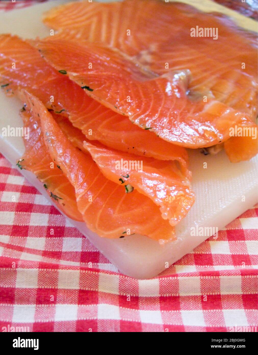 Freshly sliced pieces of gravlax on white board and gingham tablecloth - Stock Photo