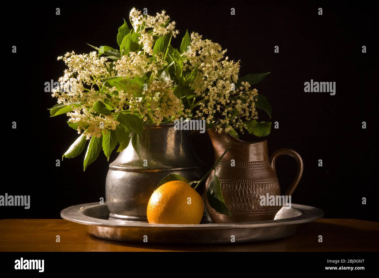 Elderflowers and orange with leaves on pewter charger with black background - Stock Photo