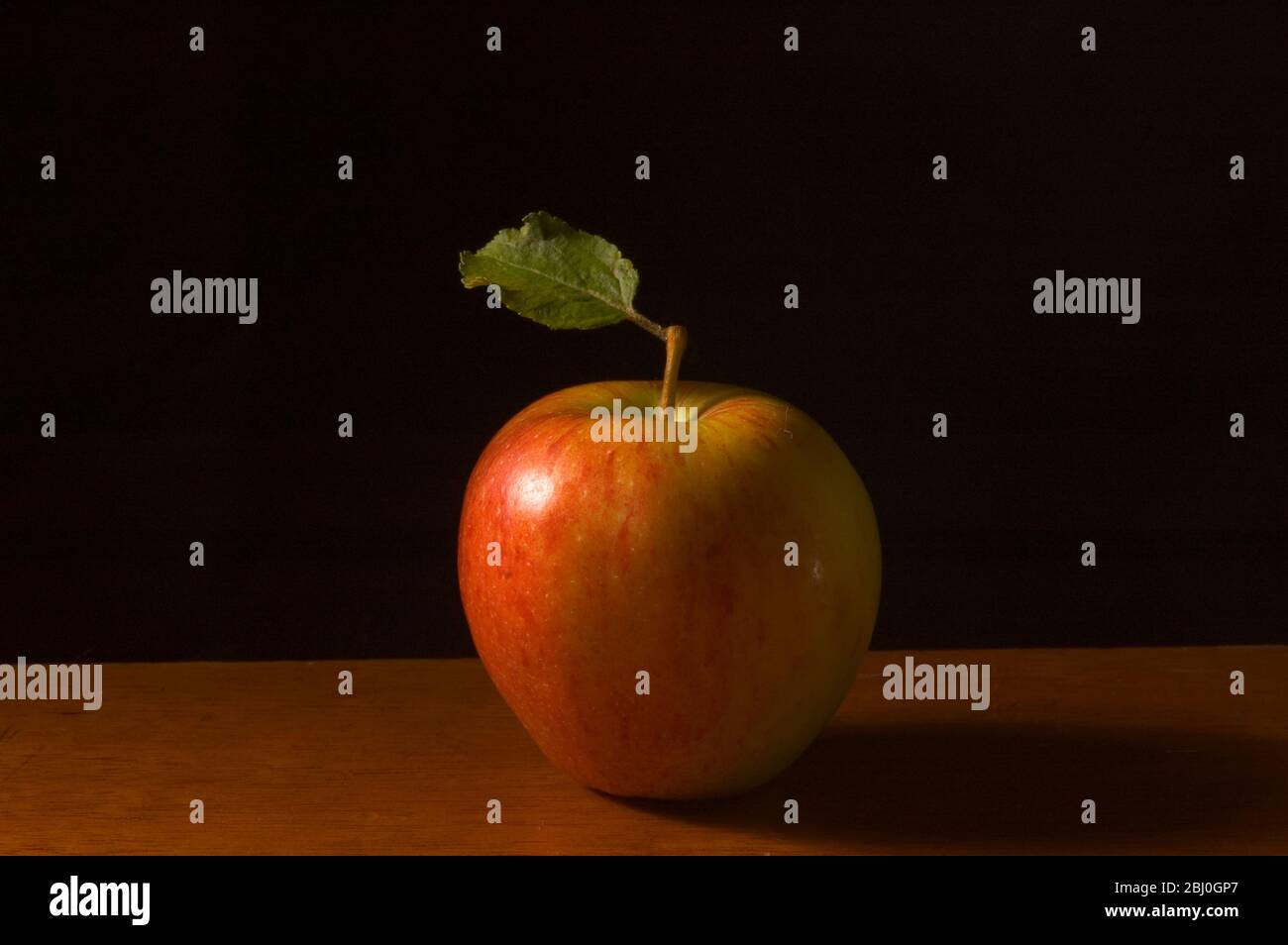 Apple with leaf on wooden surface against black background - Stock Photo