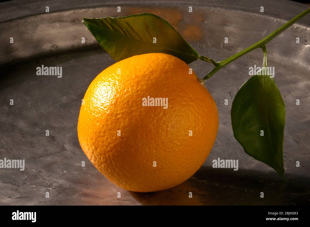 Orange with leaves on pewter charger - Stock Photo