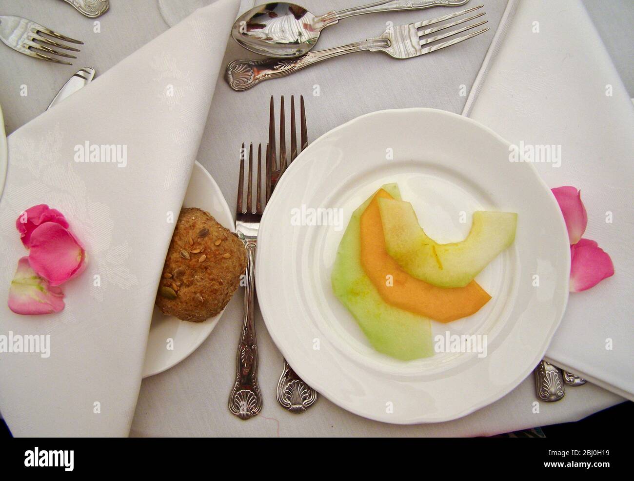 Table setting at wedding dinner with scattered rose petals on white cloth - Stock Photo