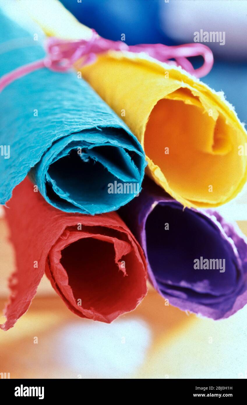 Four pieces of brightly coloured handmade paper rolled up and tied with pink string. - Stock Photo