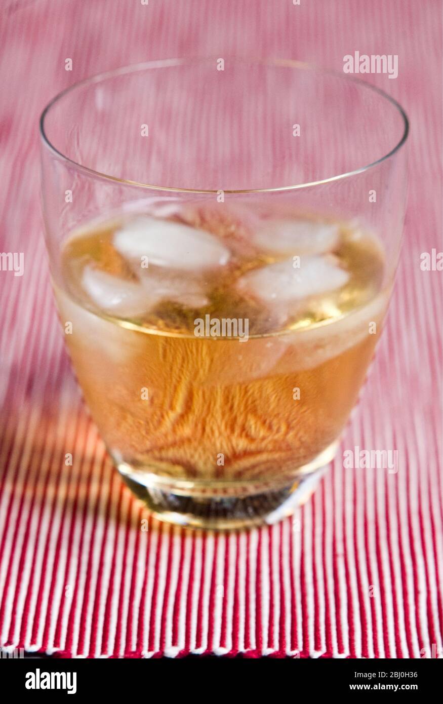 Modern glass of Scotch whisky and water with ice on red striped background - Stock Photo