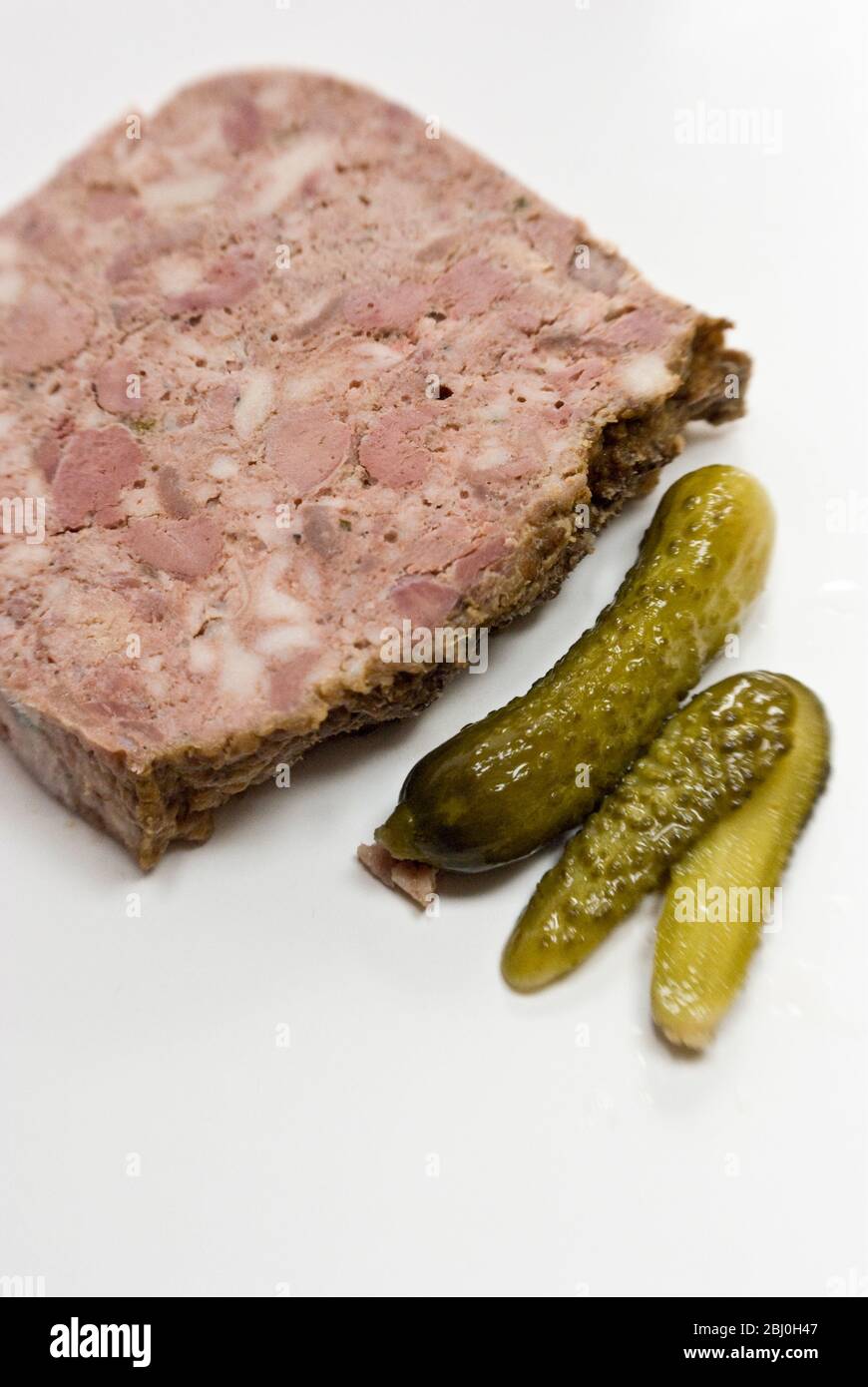 Slice of patŽ de campagne, country patŽ with little cornichon gherkins, on white plate. - Stock Photo