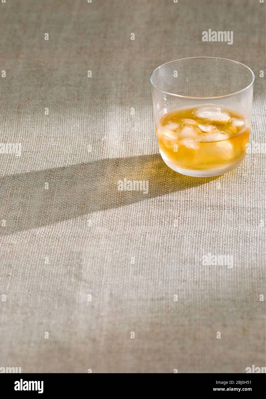 Glass of whisky with ice on rough hessian cloth - Stock Photo