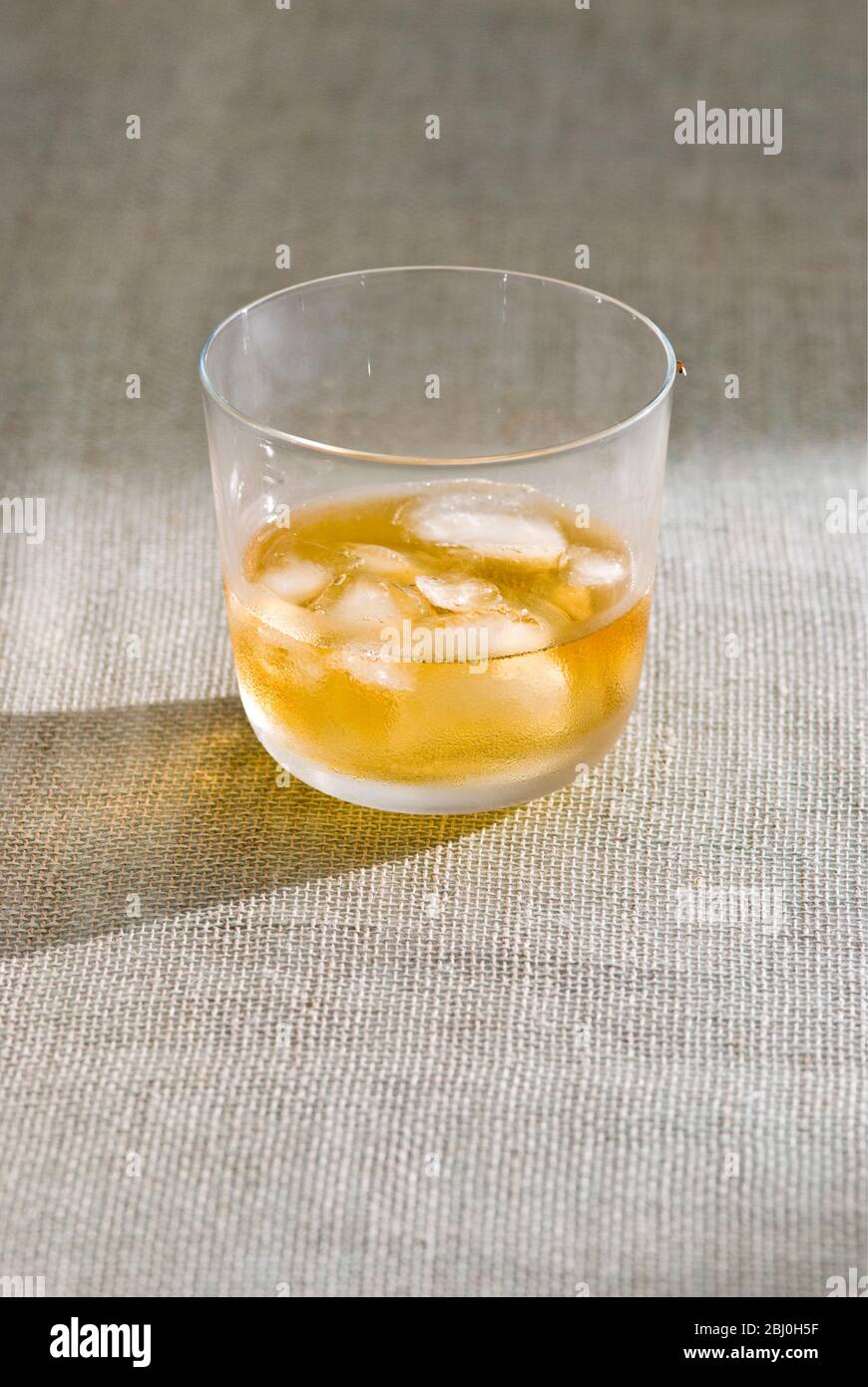 Glass of whisky with ice on rough hessian cloth - Stock Photo
