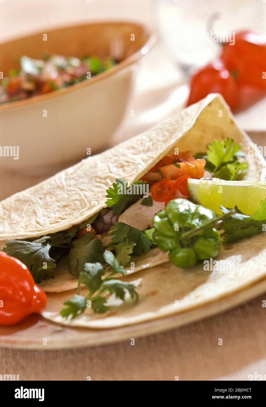 Soft flour tortilla with chicken and salsa served with lime wedges and hot red and green Scotch bonnet chilli peppers - Stock Photo