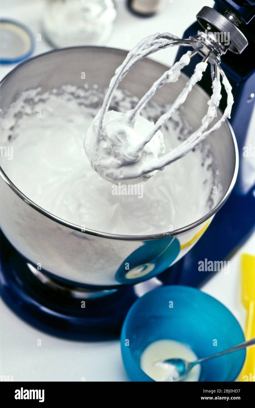 Beaten egg white in stainless steel mixer in kitchen setting, showing stiffness of the egg whites - Stock Photo