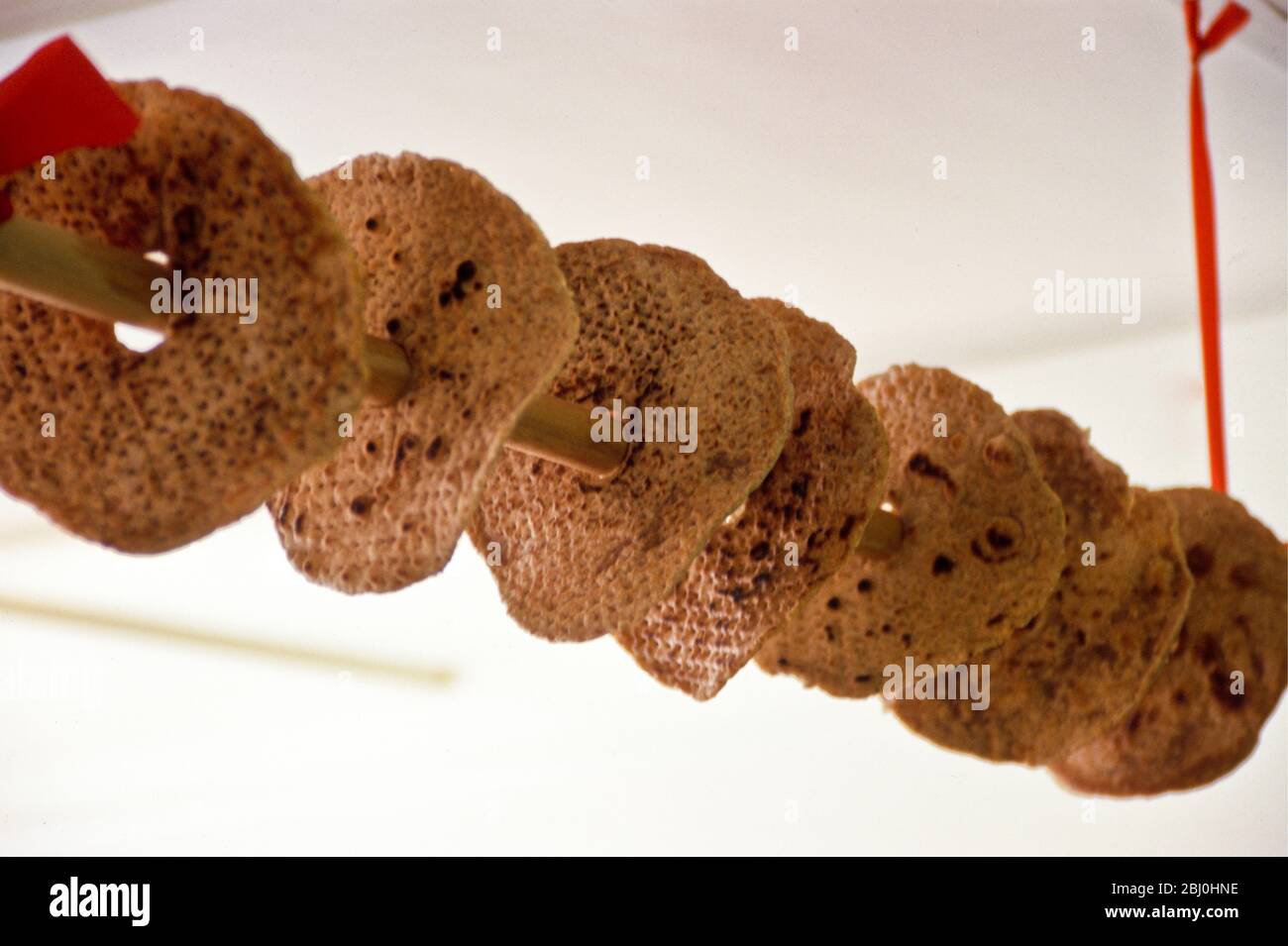 Circular cakes of handmade Swedish rye hardbread threaded onto pole suspended from ceiling to dry - Stock Photo