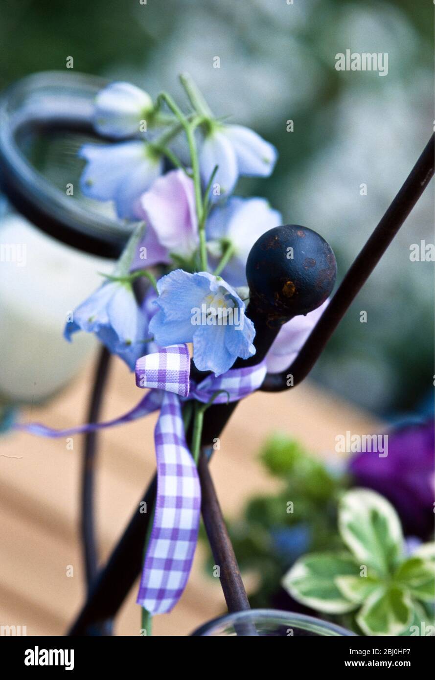 Sprig of flowers tied to metal chairback with gingham ribbon as decoration for summer evening outdoor party in garden - Stock Photo