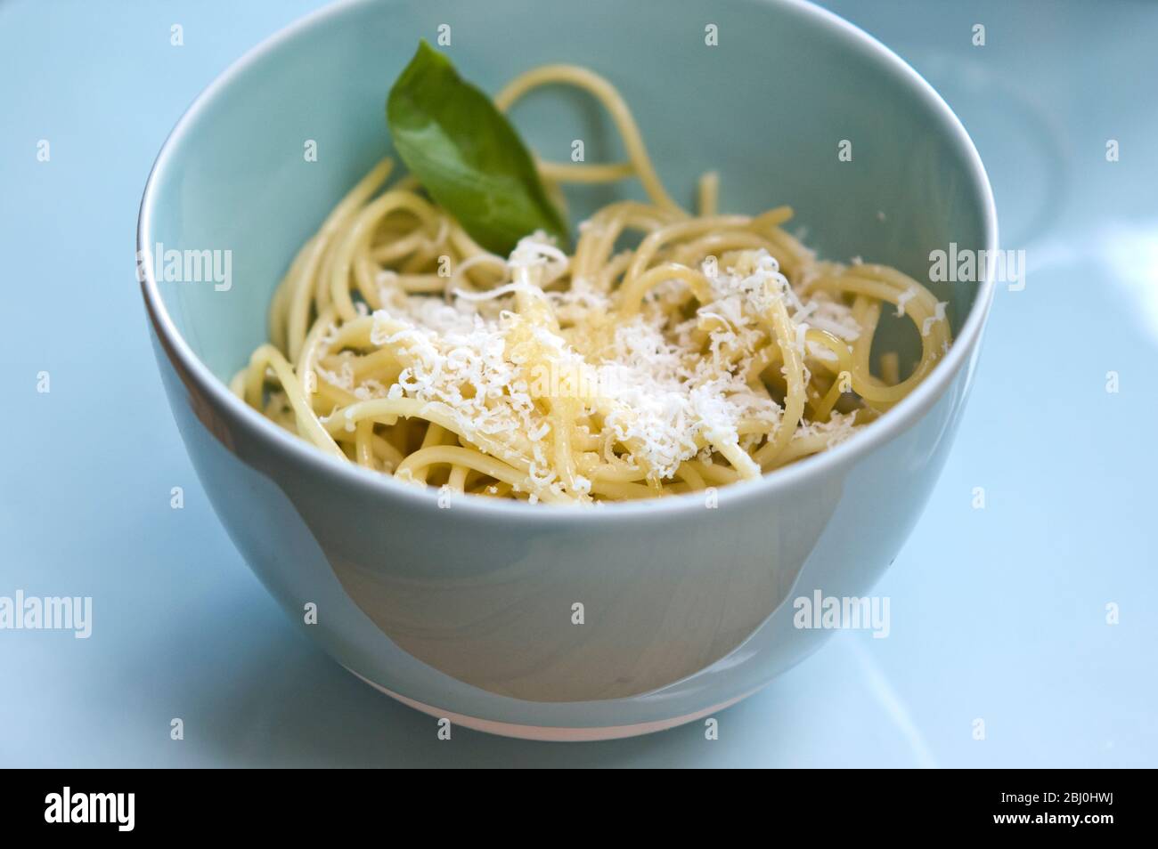 Bowl of plain spaghetti with olive oil and freshly grated parmesan in celadon bowl - Stock Photo