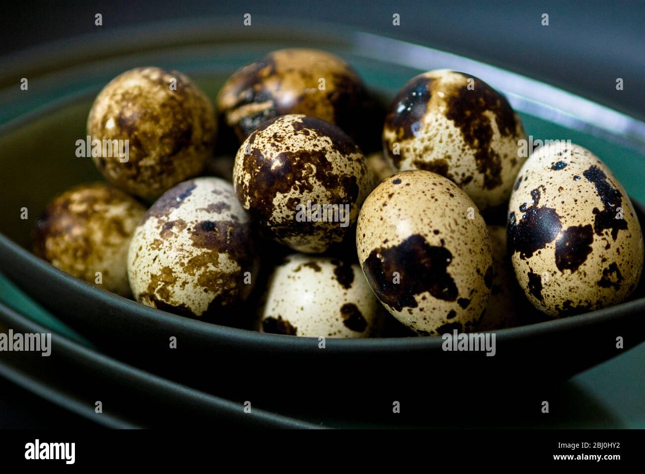 Quail's eggs in their shells in dark green bowls stacked - Stock Photo