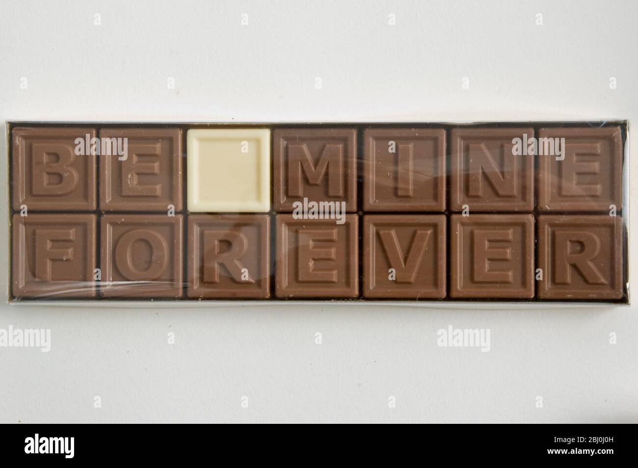 Chocolate letters spelling 'Be Mine Forever' in cellophane box as Valentine's day gift - Stock Photo
