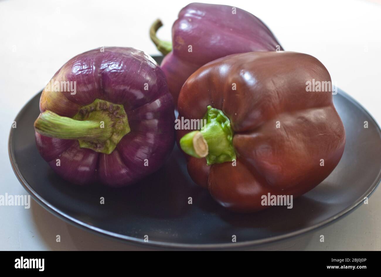 Purple and brown sweet peppers on black plate - Stock Photo