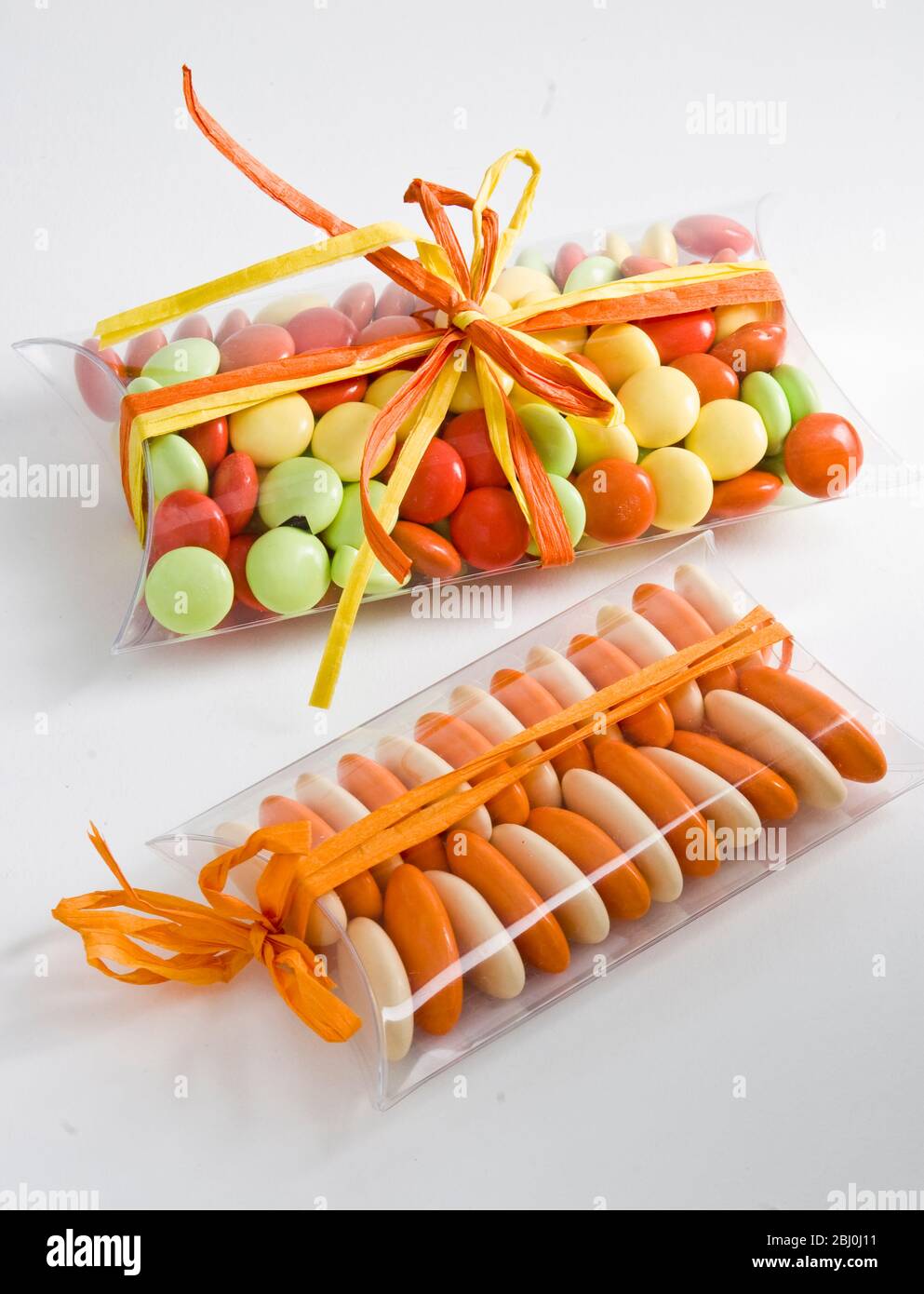 Multi coloured amond and chocolate sugar coated dragees, in cellophane boxes tied with ribbon - Stock Photo