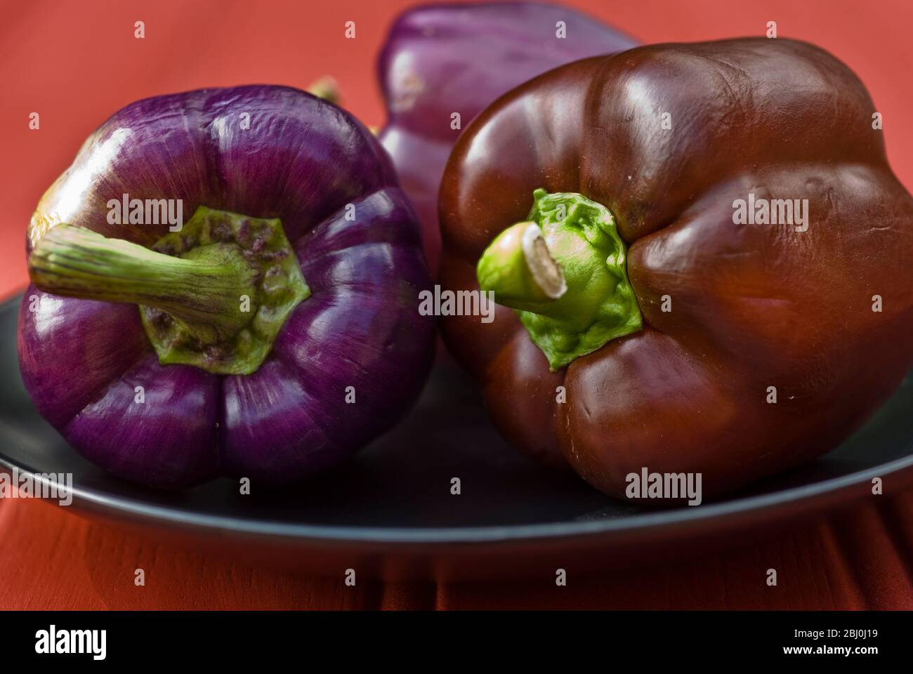 Purple and brown sweet peppers on black plate - Stock Photo