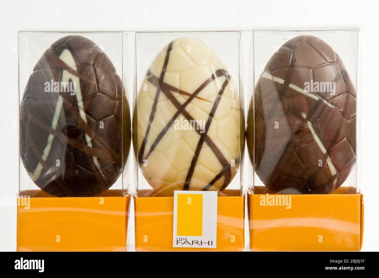 Three similar chocolate Easter eggs - plain, whie and milk chocolate, in cellophane boxes. - Stock Photo