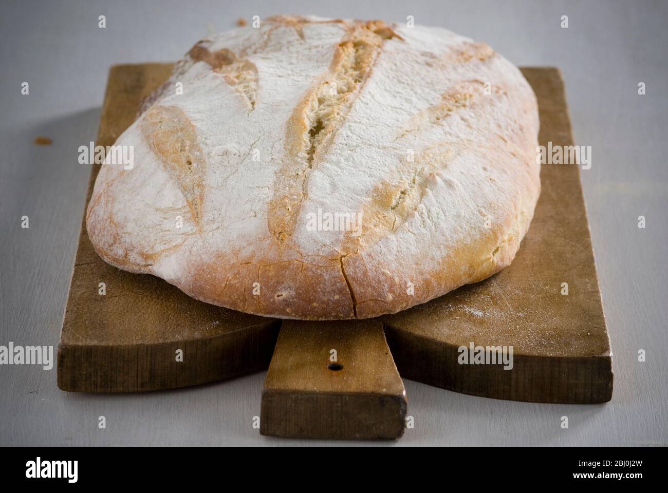 Organic rustic white loaf on wooden cutting board - Stock Photo