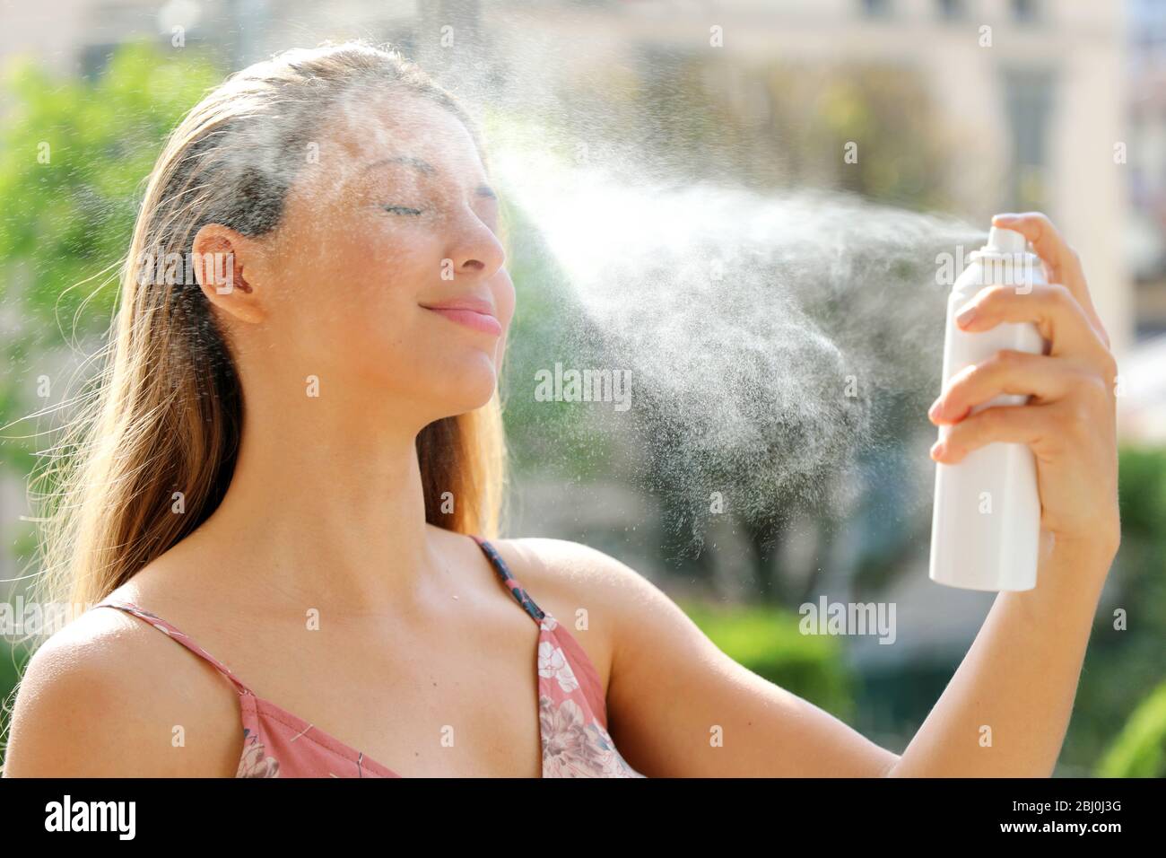 Young woman spraying Thermal Water on her face outside. Thermal water used for skin care, fix makeup, help skin irritation, redness and insect bites. Stock Photo