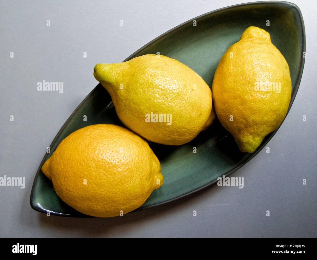 Three lemons on green plate - Stock Photo
