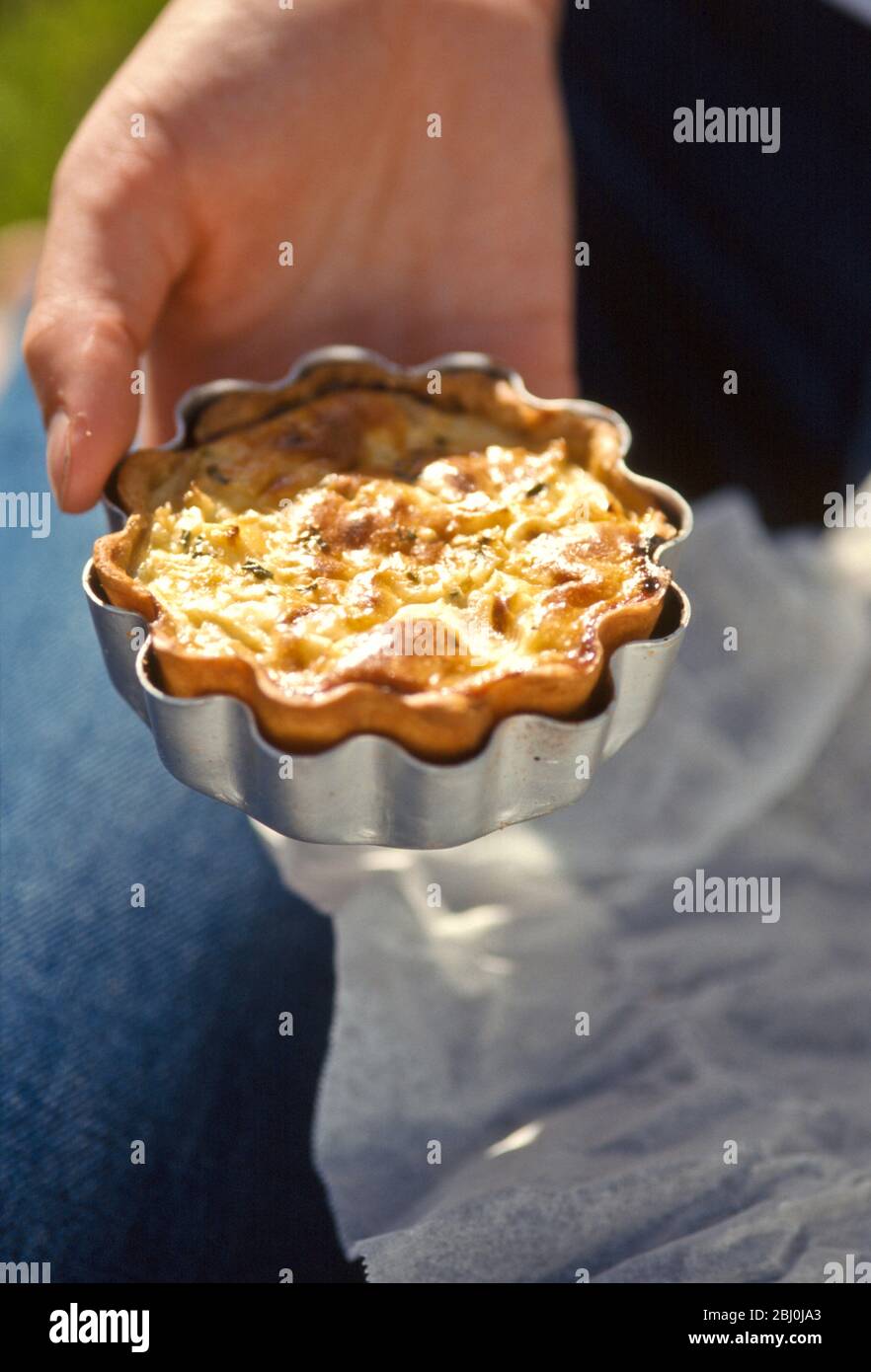 Home made quiche in its tin held in the hand - Stock Photo