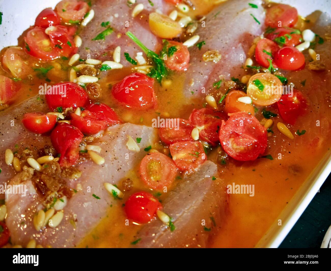 Fillets of seabass with pinenuts, parsley, cherry tomatoes and olive oil, before being put in oven. - Stock Photo