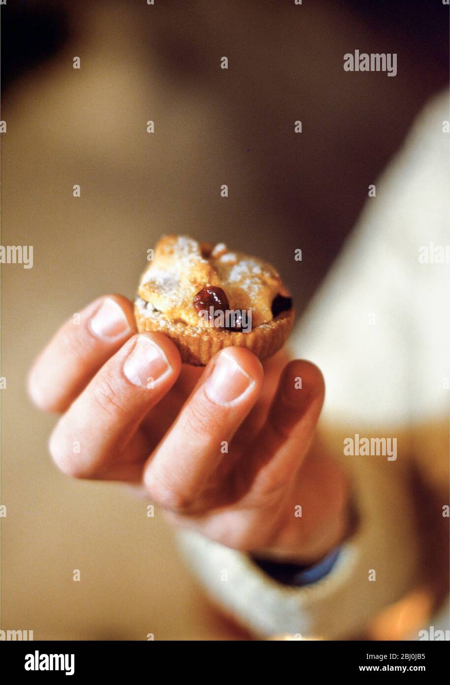 Hand holding mini cranberry mincepie outdoors in snow - Stock Photo