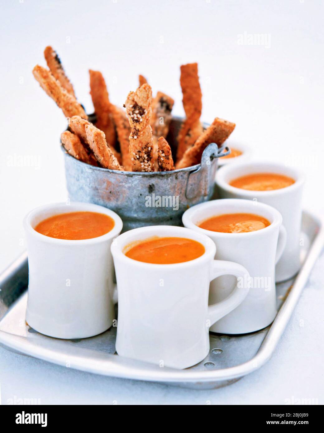 Tray of warming mugs of hot tomato soup with metal bucket of seeded cheese straws - Stock Photo