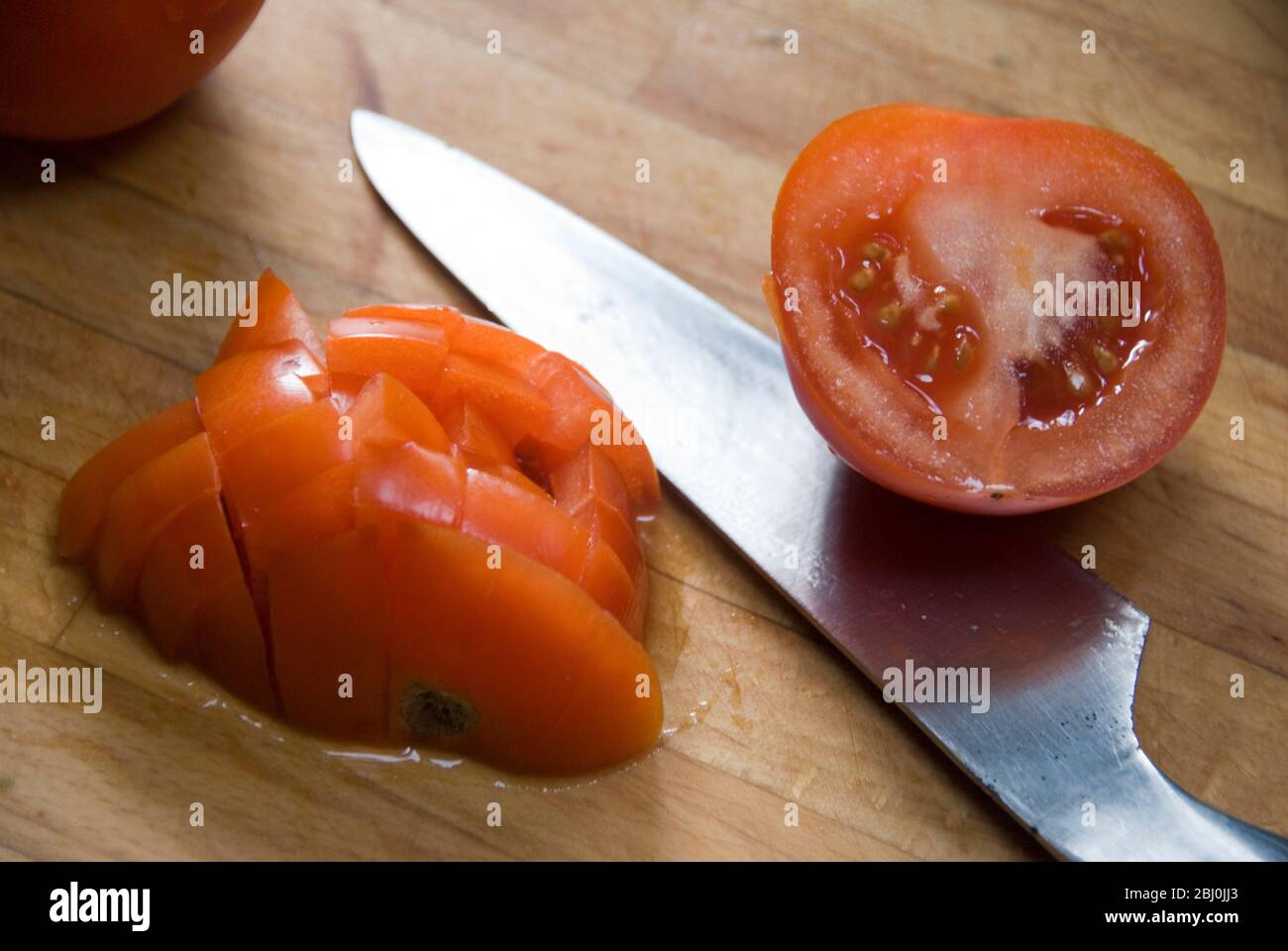 Chopping fresh tomatoes on wooden chopping board with sharp Global knife Stock Photo