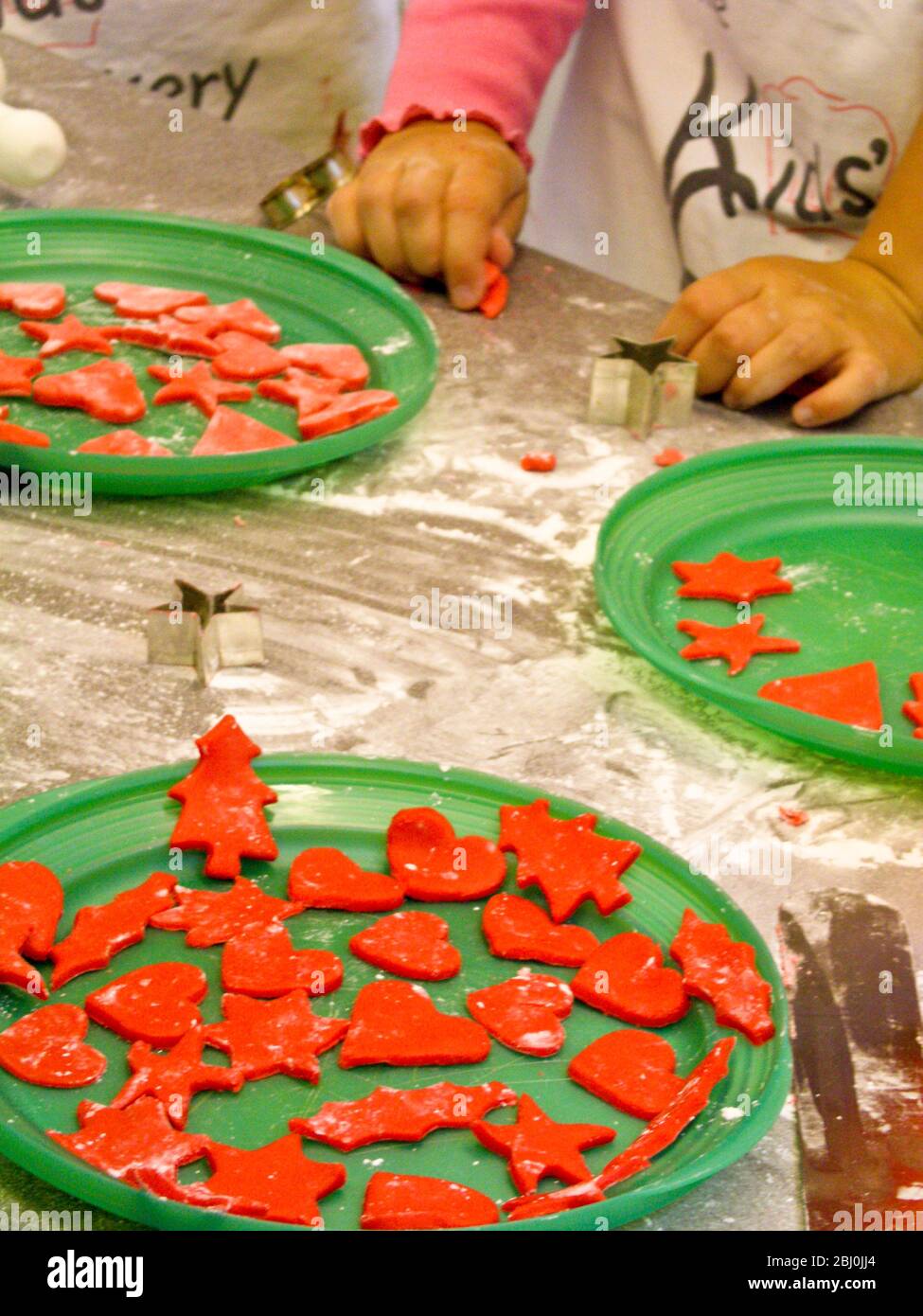 Children cutting out decorative Christmas shapes out of coloured fondant icing to decorate cakes - Stock Photo