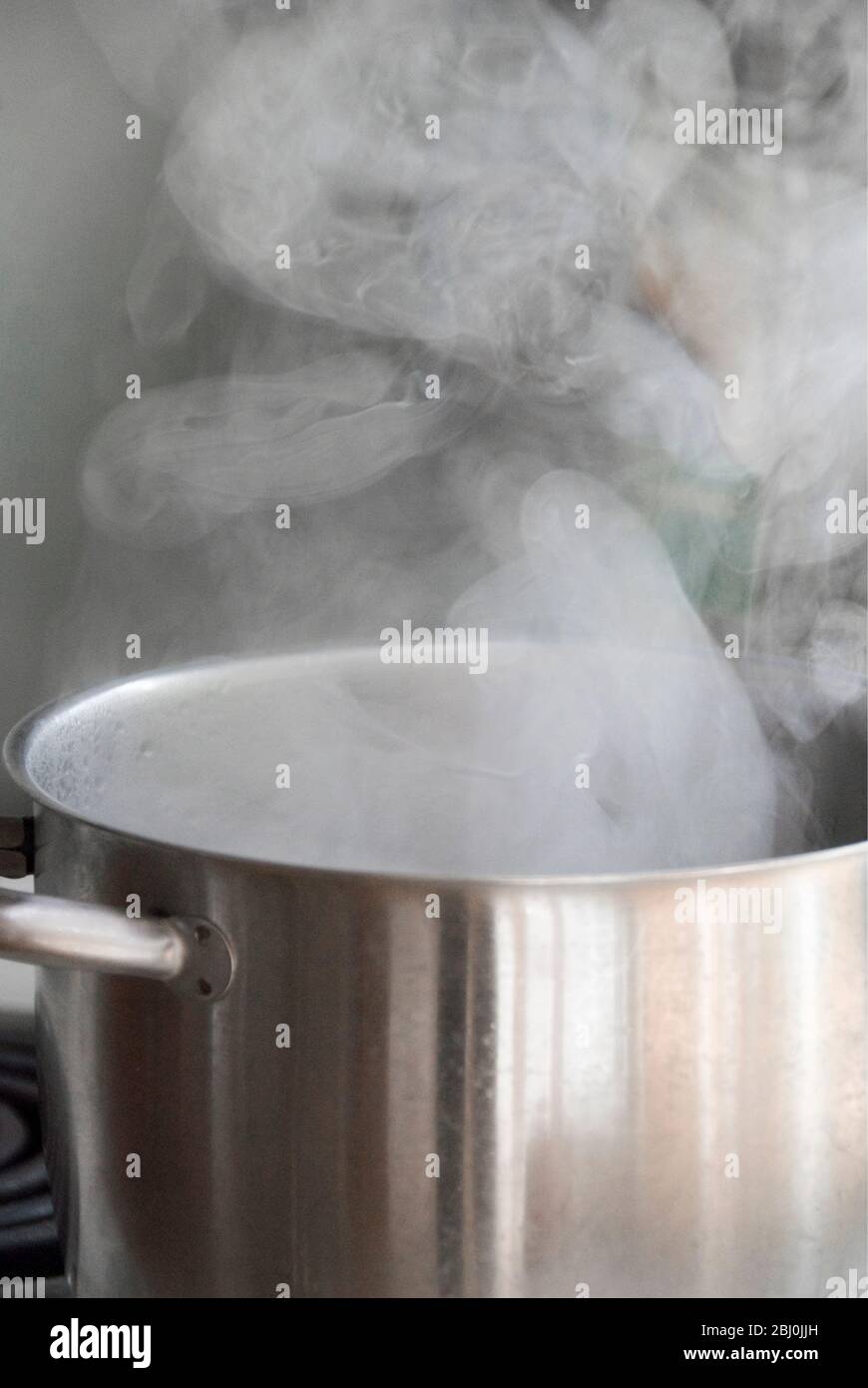 Steam from water boiling in stainless steel saucepan on hob - Stock Photo