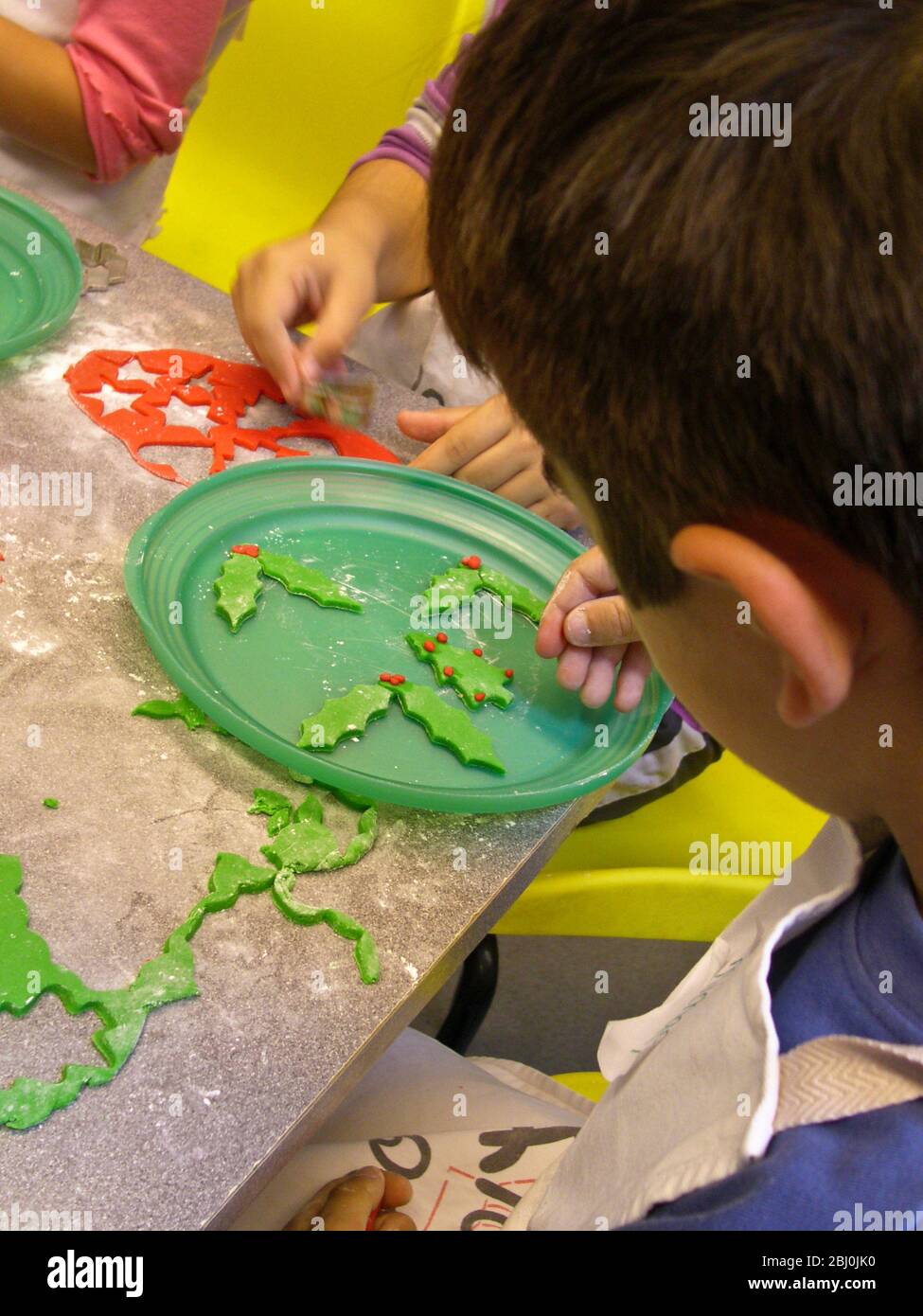Children cutting out decorative Christmas shapes out of coloured fondant icing to decorate cakes - Stock Photo
